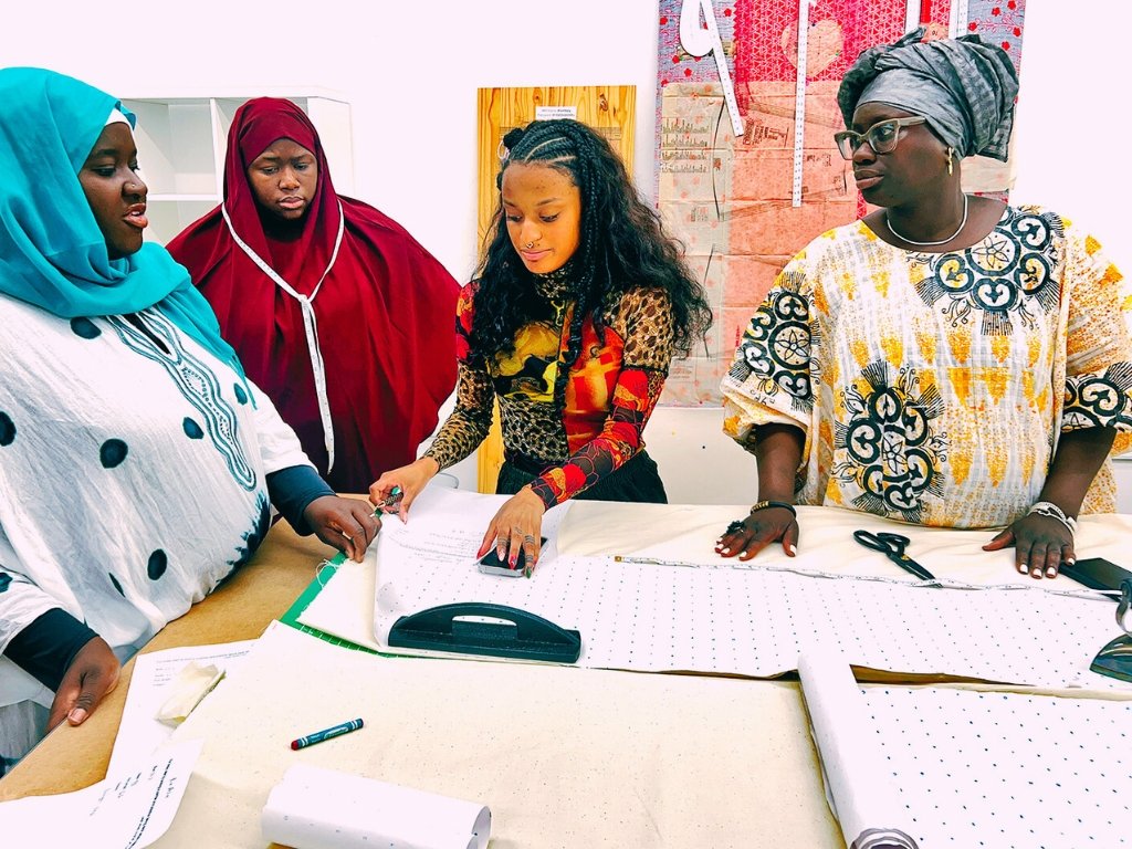 Four women of various backgrounds stand around a table